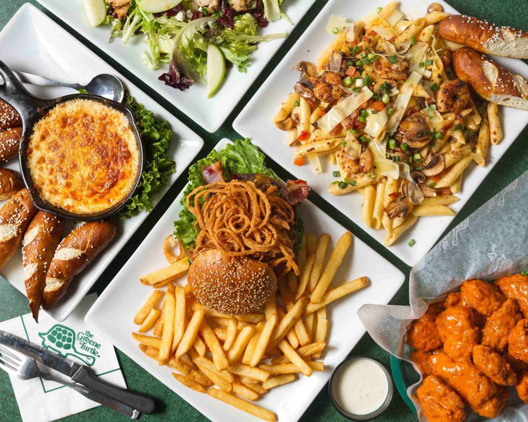 Several plates of different foods, including a burger with fries and pasta