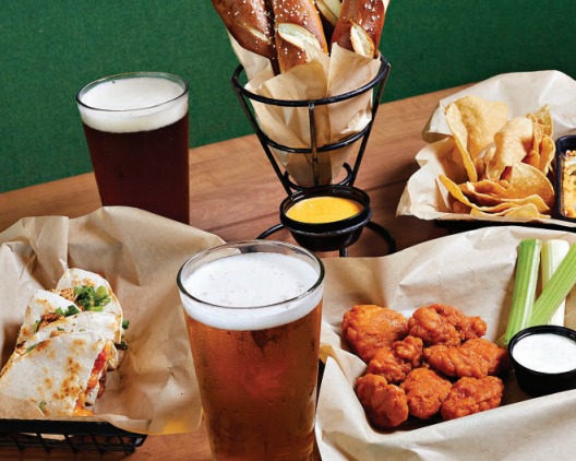 Several plates of food, including wings and chips, with glasses of beer