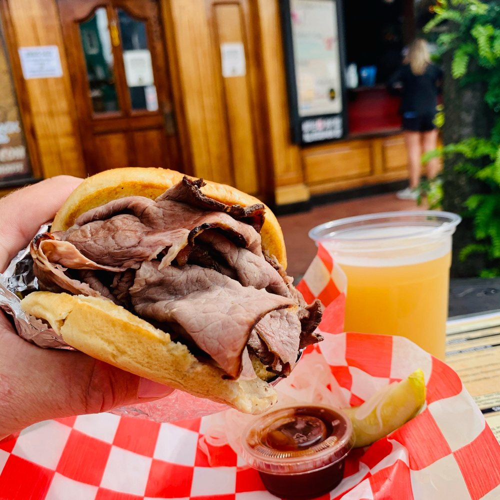 A hand holding a pit beef burger with a drink