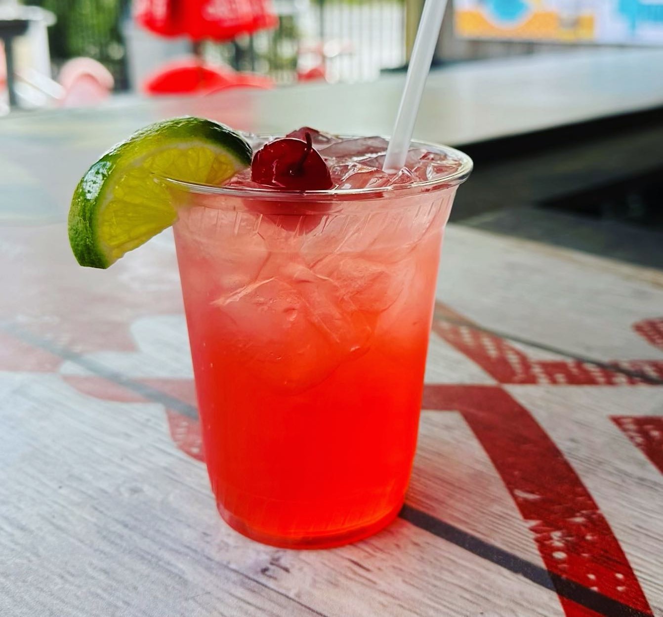 a red cocktail with a cherry and lime wedge