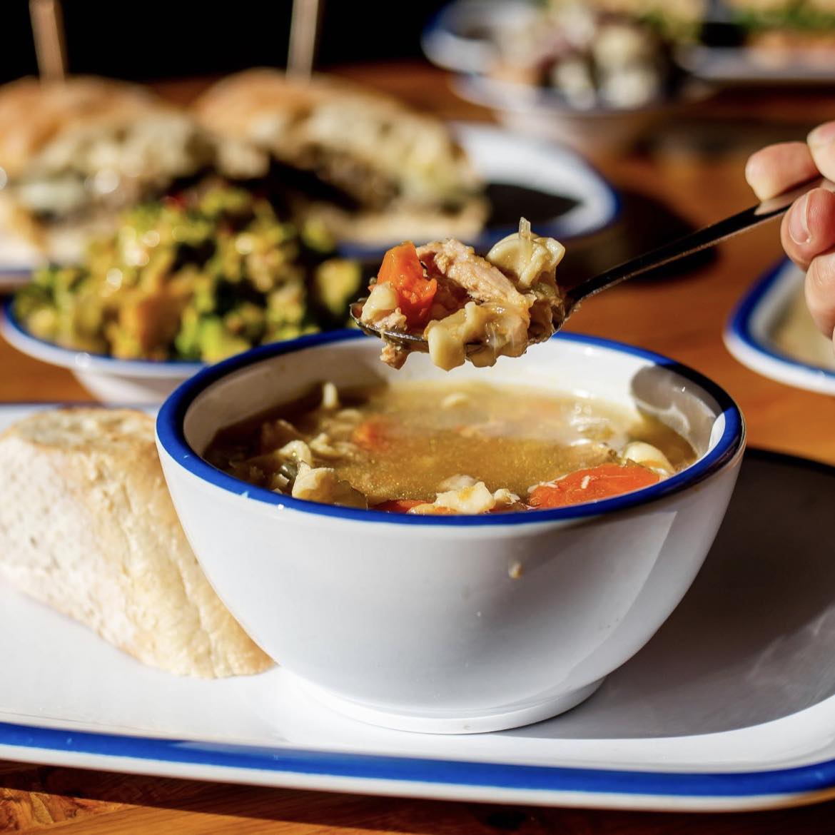 a bowl of soup with other plates of food out of focus in the background