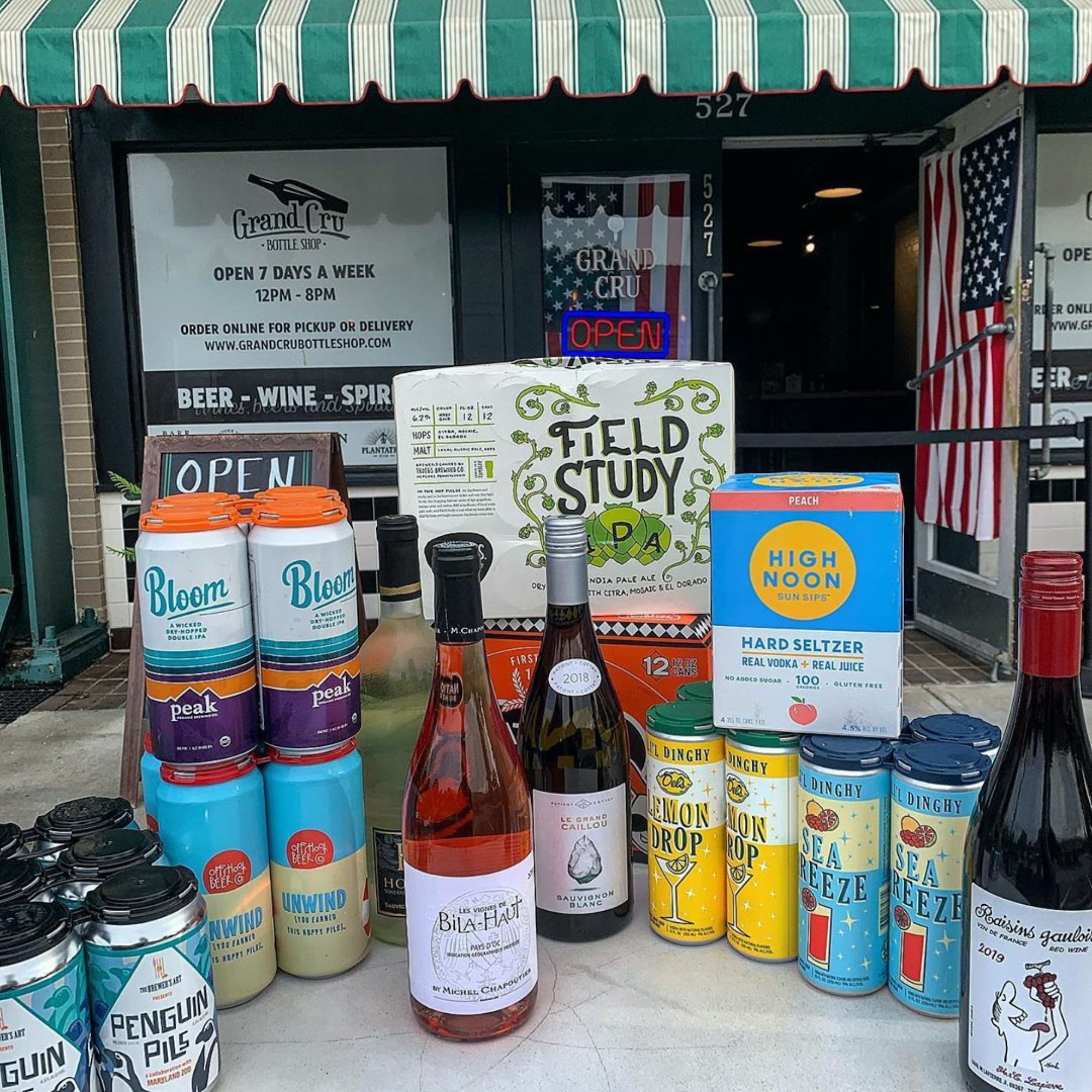 a table full of cans of beer, bottles of wines, and other beverages in front of grand cru bottle shop