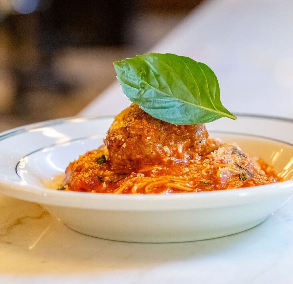 a plate of spaghetti and a meatball with a basil leaf