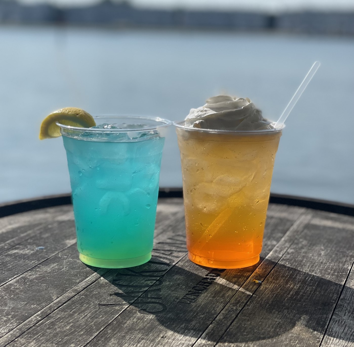 a light blue drink with a lemon wedge and an orange drink with whipped cream