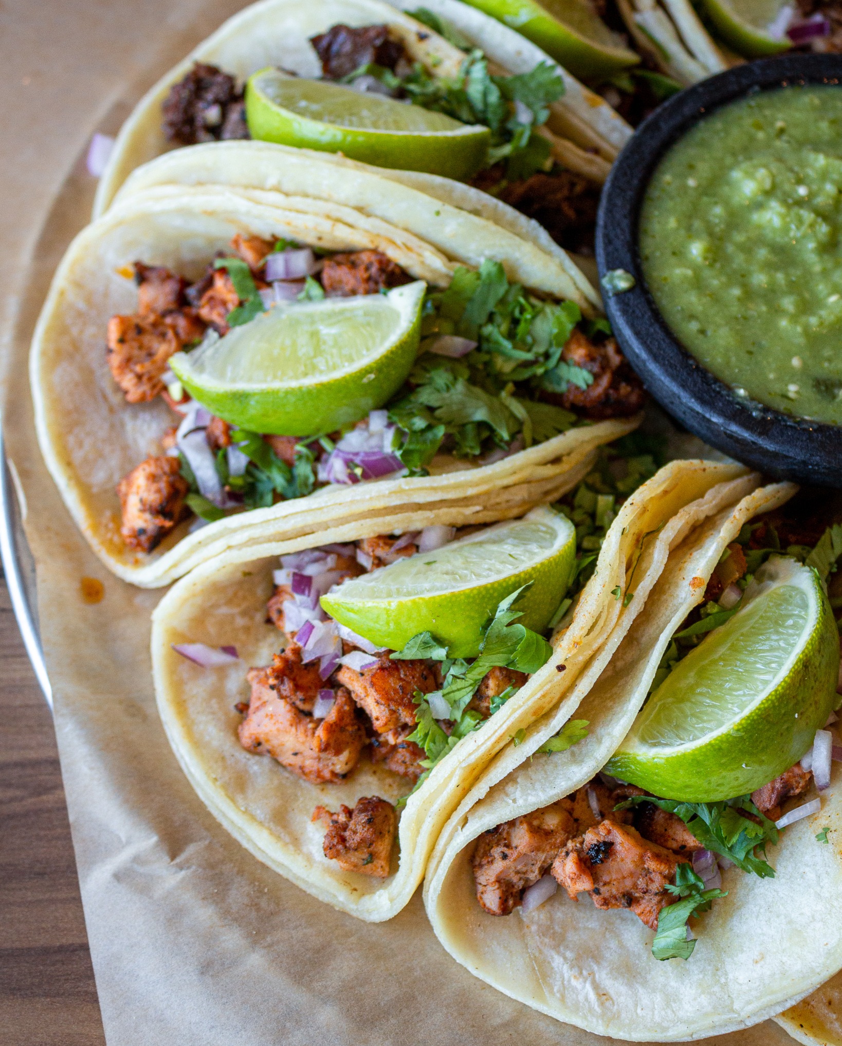 a platter of soft shell tacos with lime wedges and guacamole