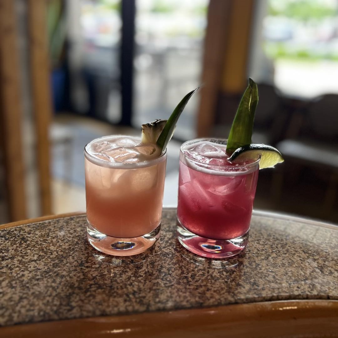 a kiwi guava margarita with a pineapple wedge and a blueberry margarita with a lime wedge