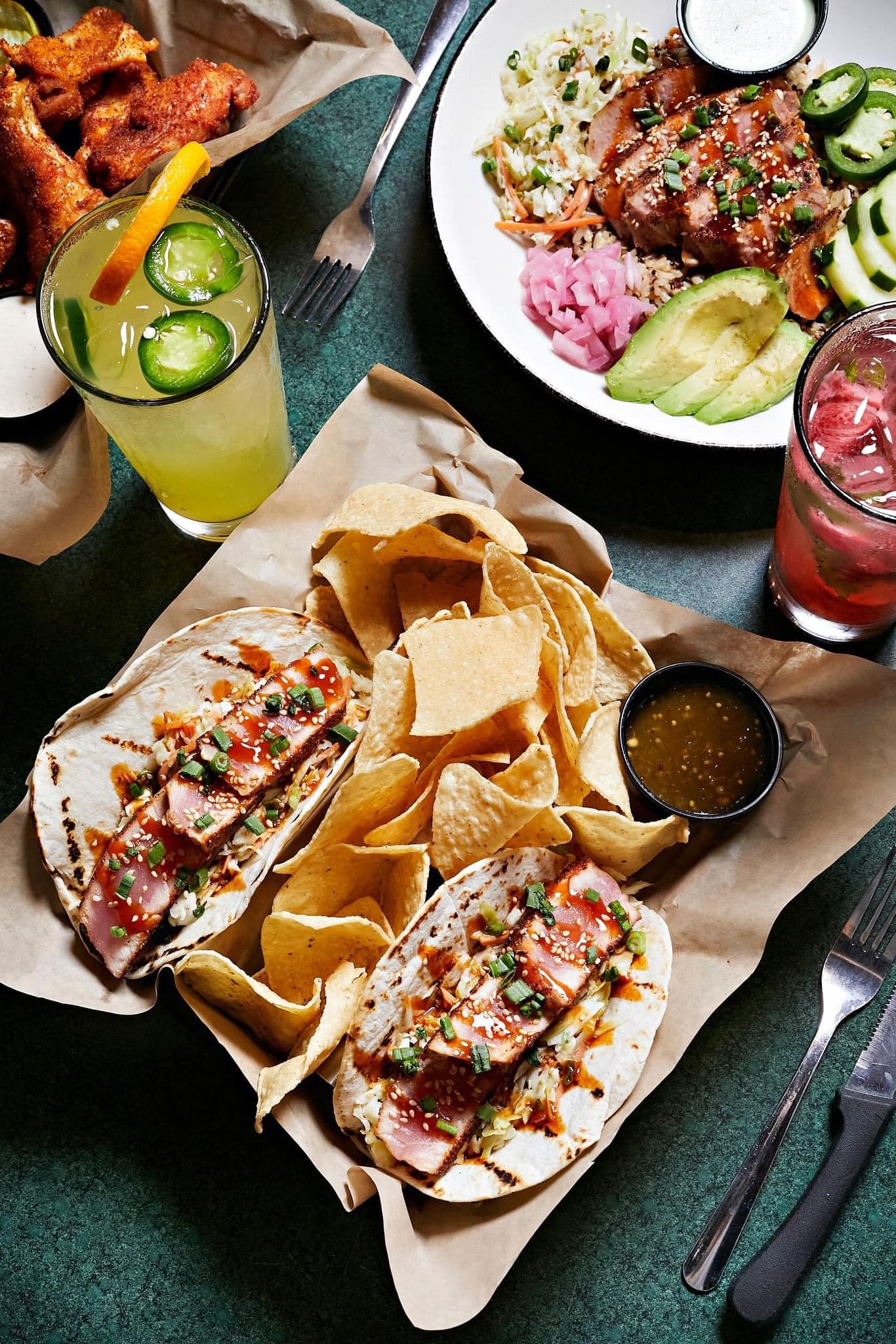 several plates of food, including tacos, with two drinks