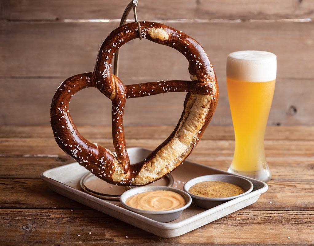 a soft pretzel with dips and a glass of beer