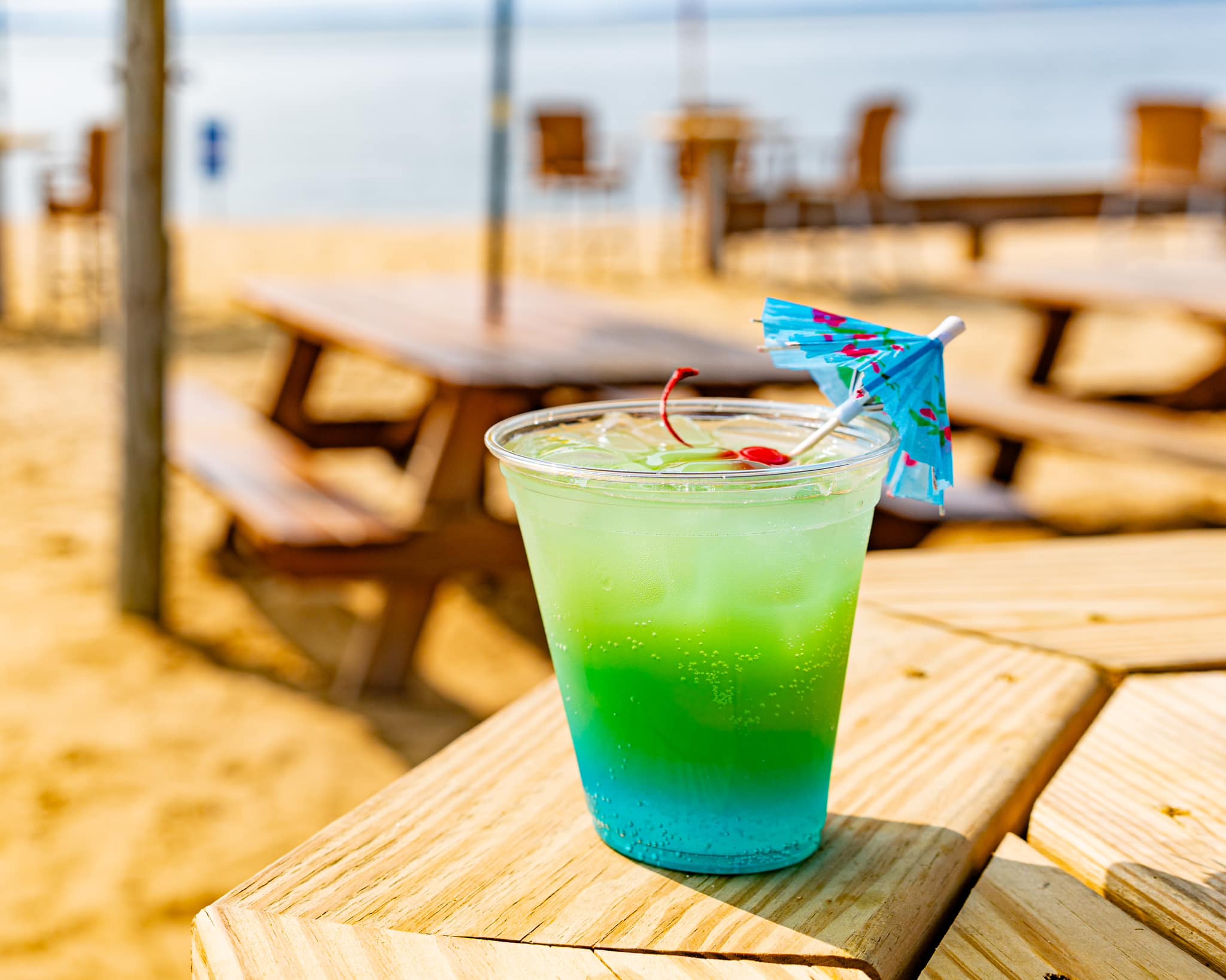 a blue and green cocktail with a cherry and an umbrella