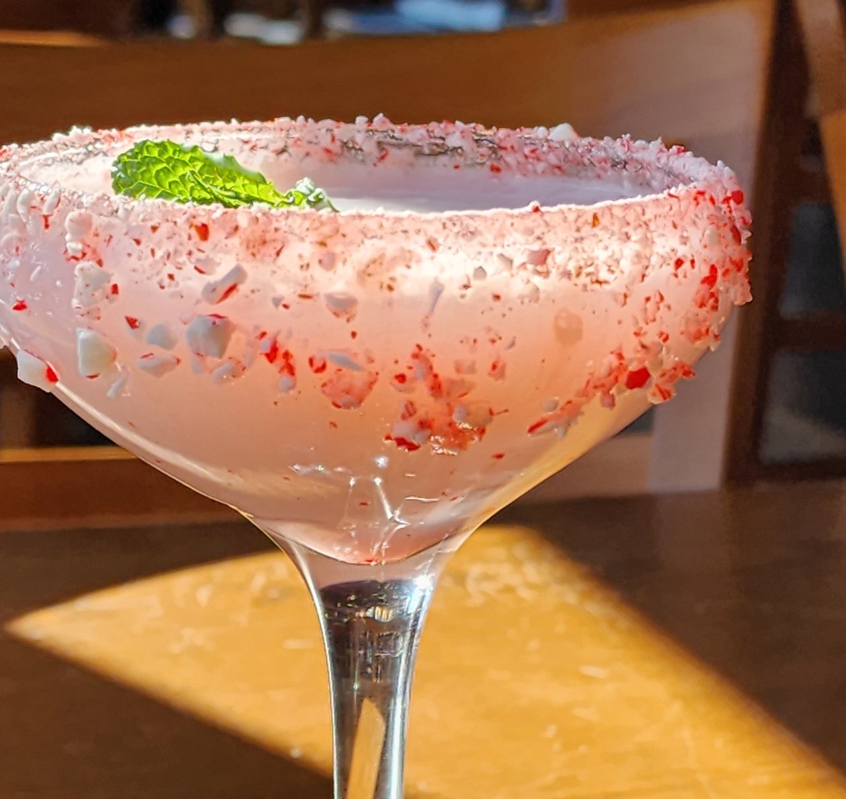 a candy cane swirl cocktail with a candy cane rim and a sprig of mint