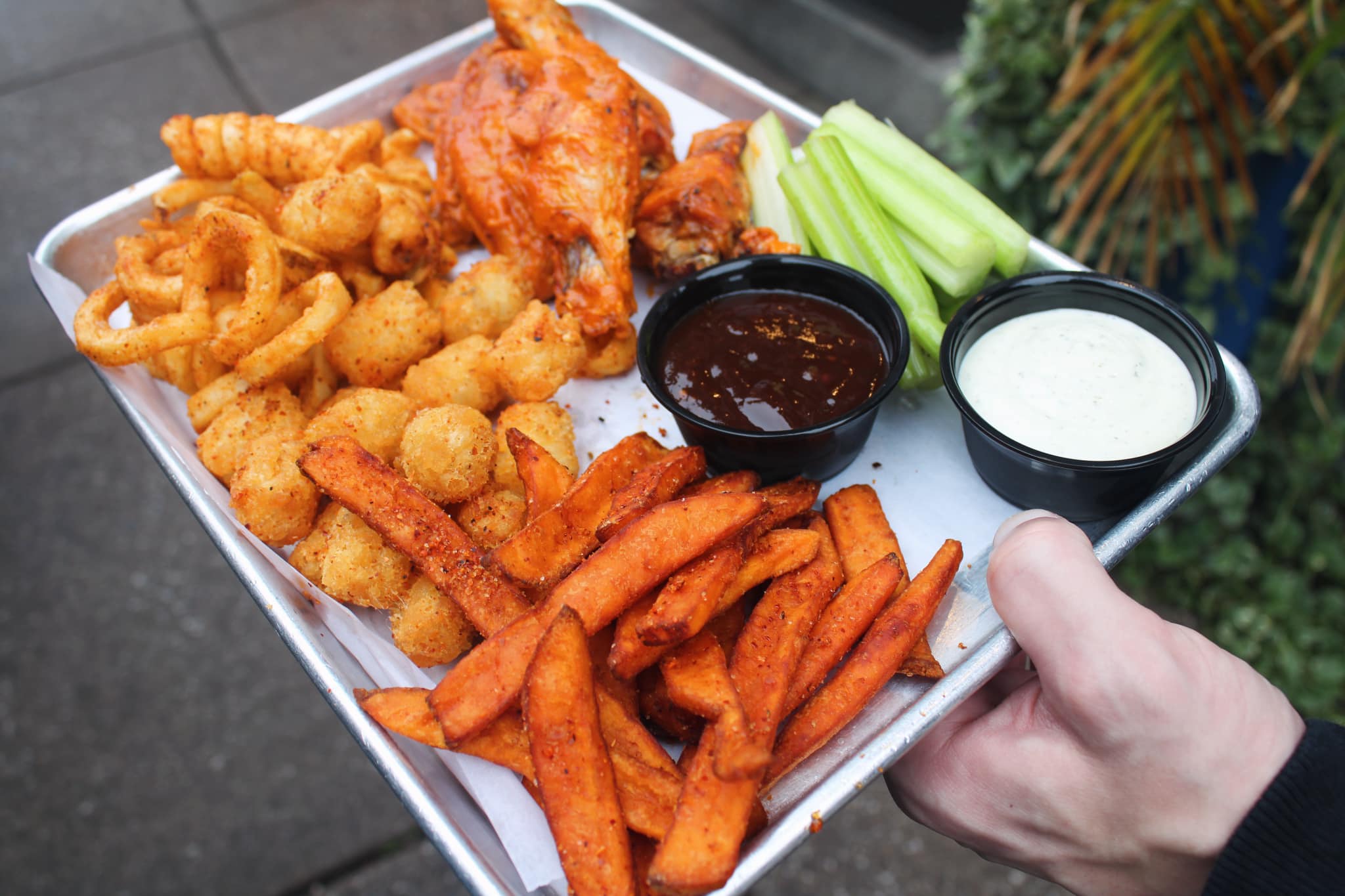 a platter of wings with celery, curly fries, sweet potato fries, tater tots, and dips