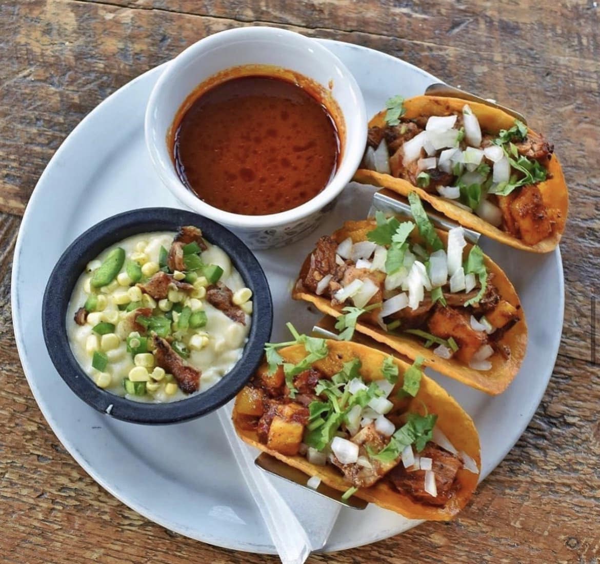 a plate of three al pastor tacos with birria broth & smokey queso blanco