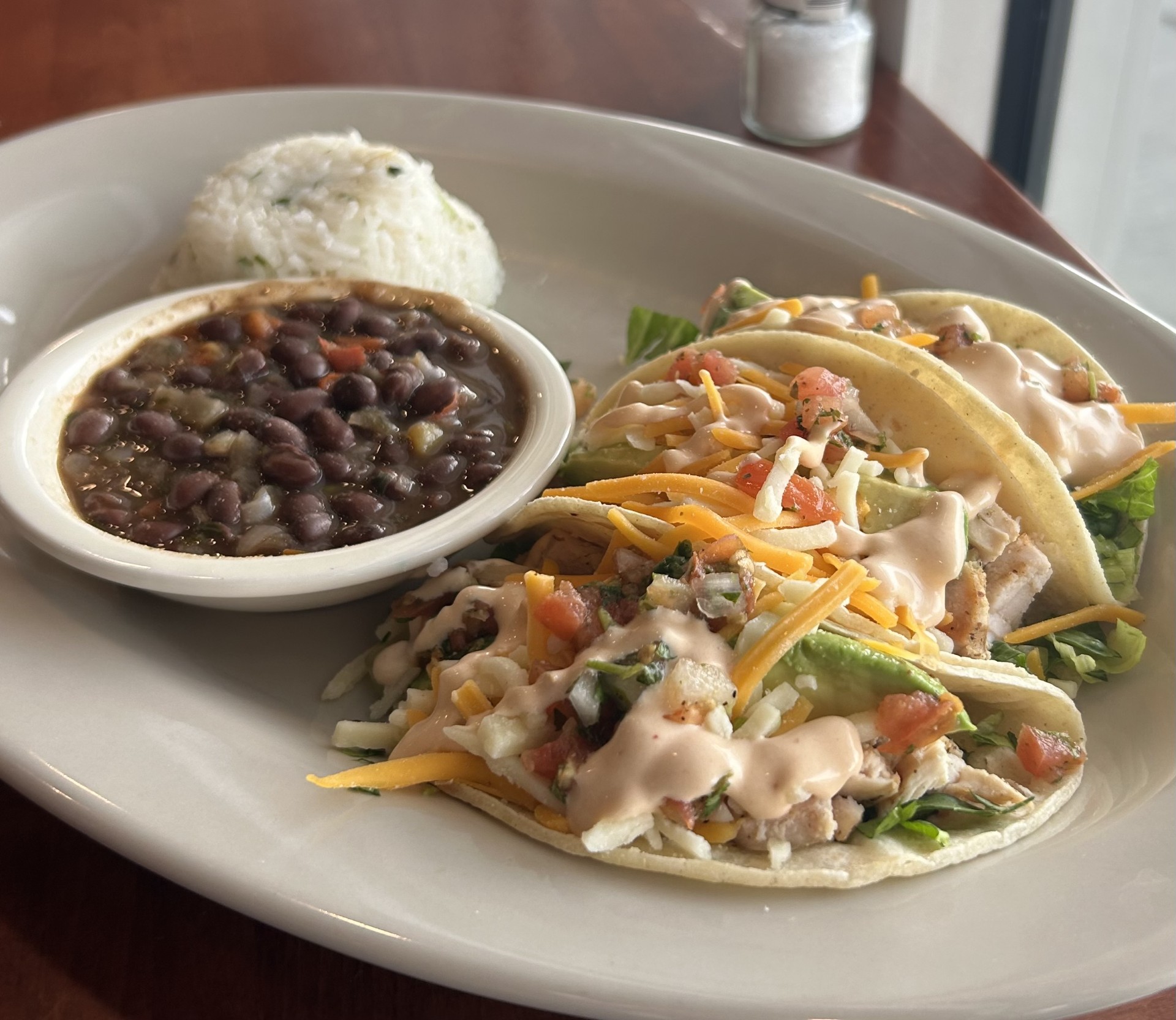 a plate with three soft shell tacos, black beans, and cilantro rice