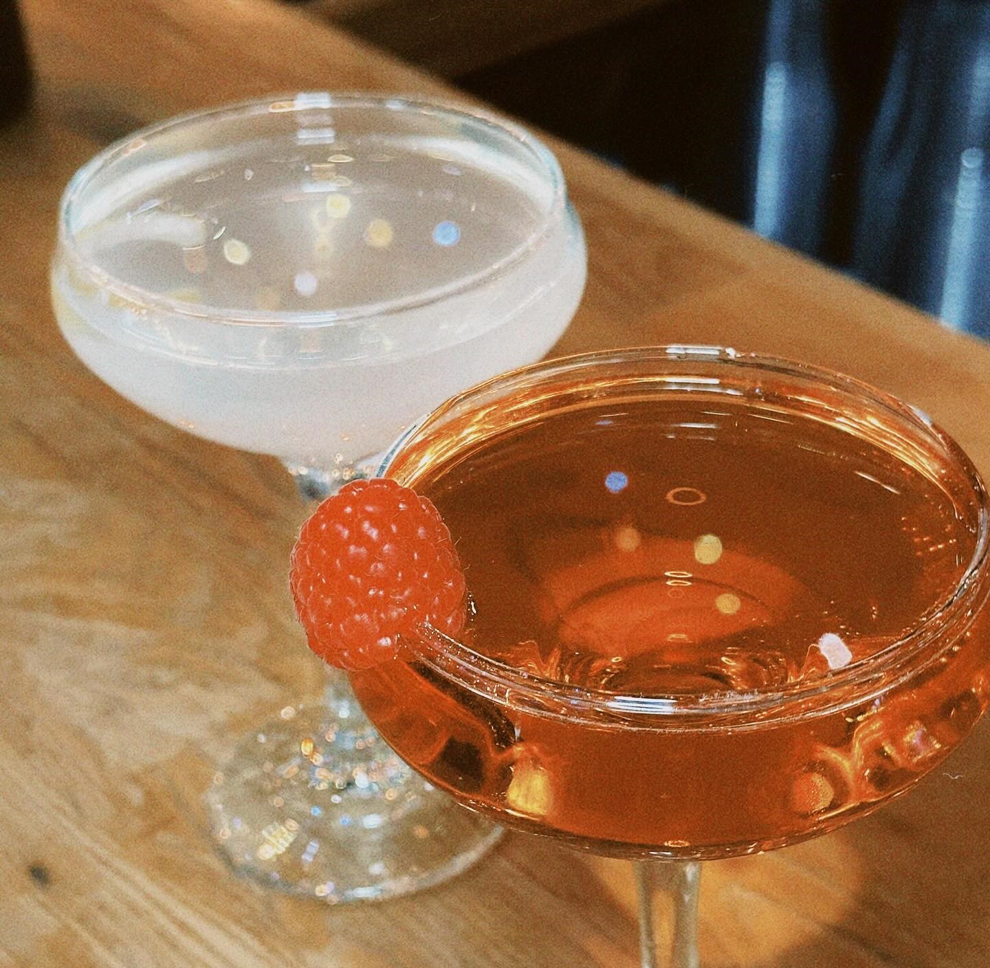 two cocktails, one clear, and one reddish with a raspberry