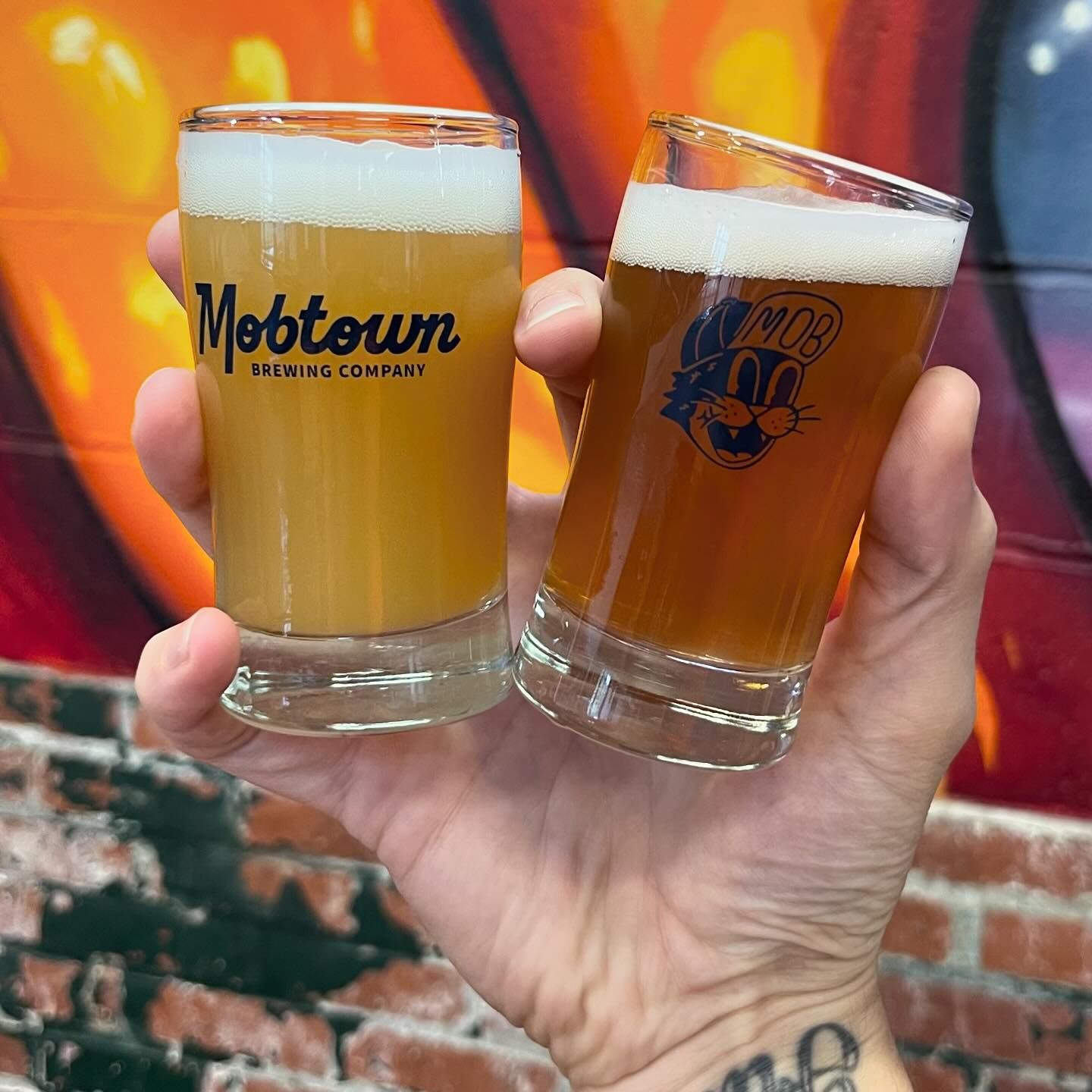 a hand holding two mobtown shot glasses of beer