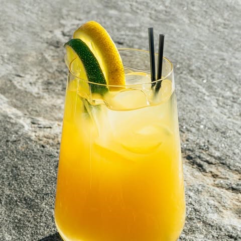 a yellow orange cocktail with a lemon & a lime slice