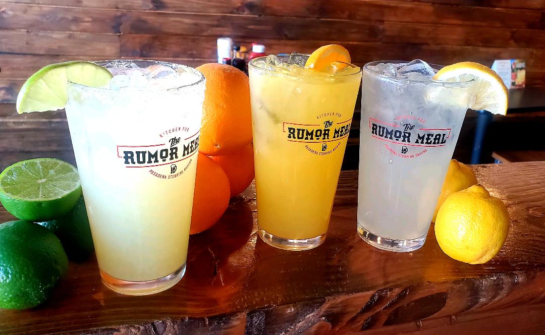 three cocktails, one yellow with a lime wedge, one orange with an orange wedge, and one clear with a lemon wedge