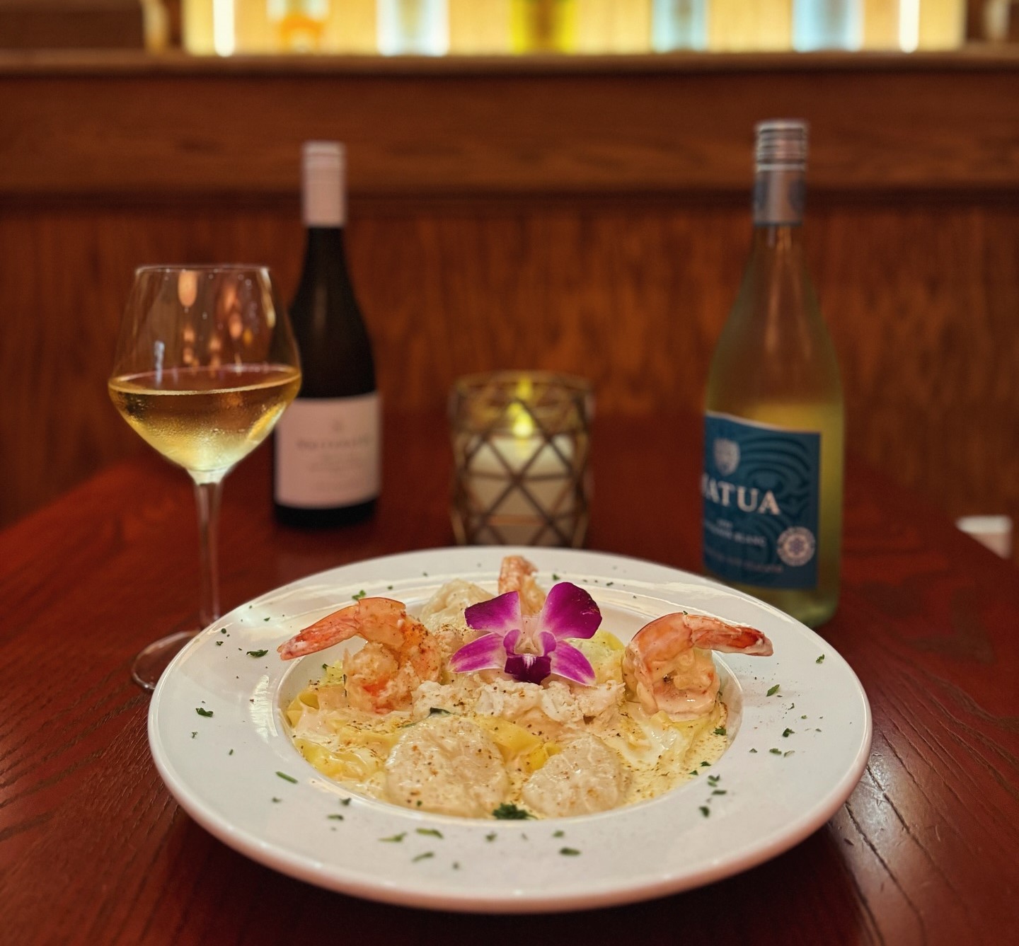a plate of seafood fettuccine with a glass of wine