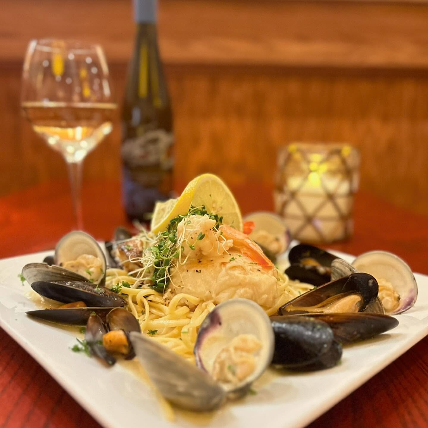a plate of seafood pasta with a glass of wine