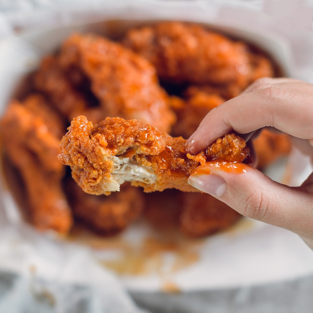 a hand holding a wing with a basket of wings in the background