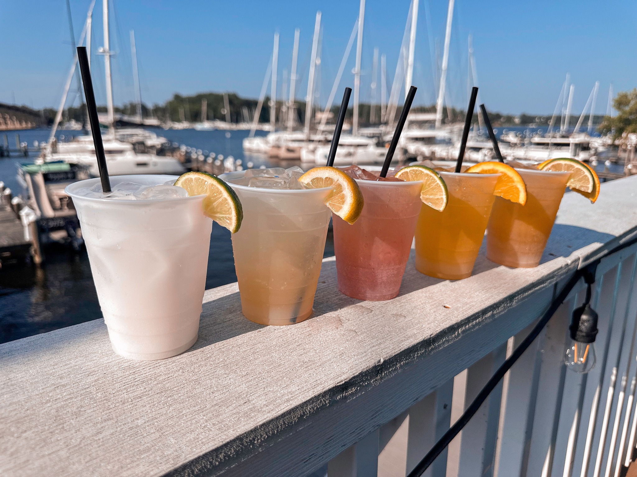five cocktails with various citrus wedges lined up on a fence outside