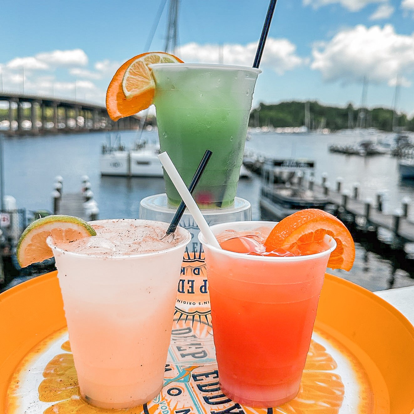 three different colored cocktails with various citrus wedges and straws on a table outside